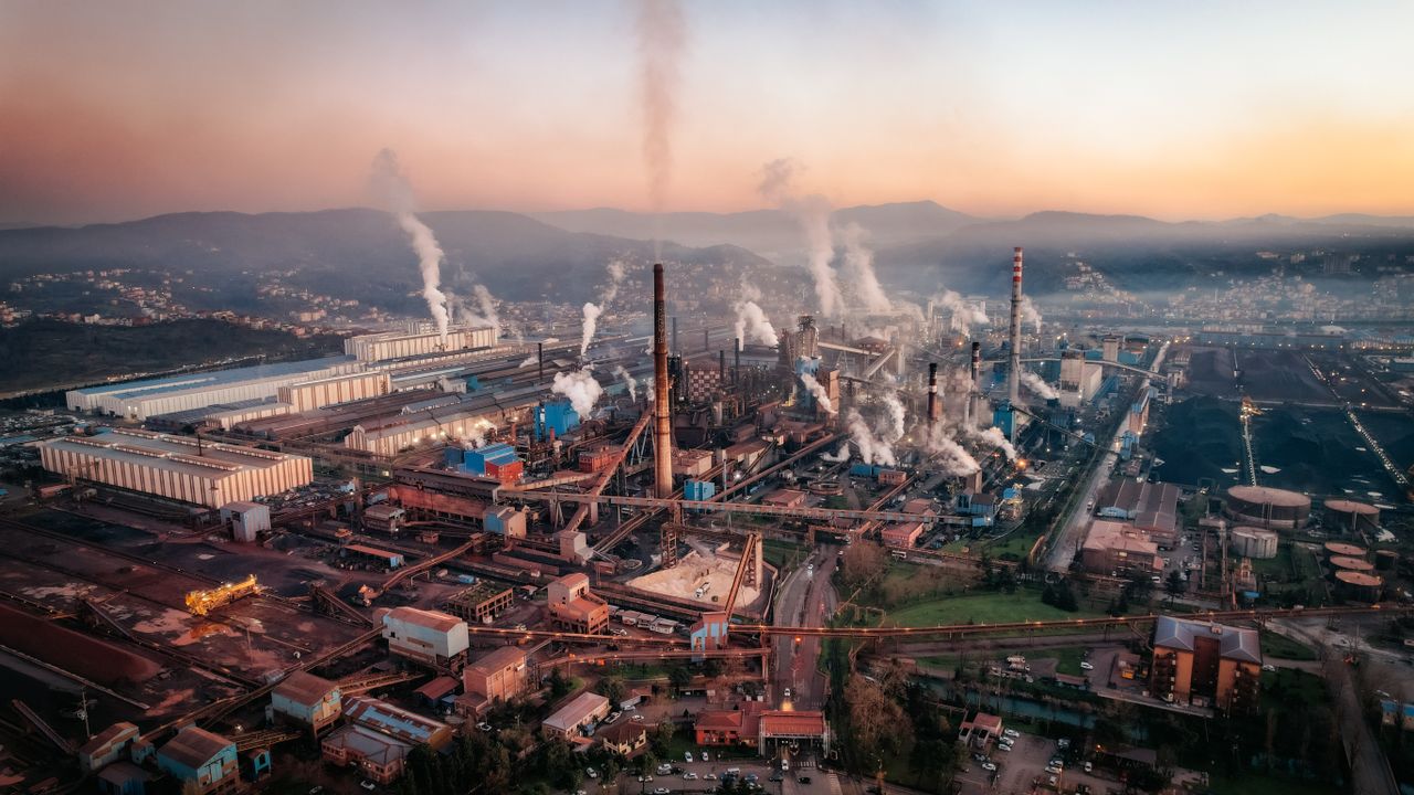 services-01 Aerial view of a factory with chimneys emitting smoke during sunset, highlighting industrial pollution.