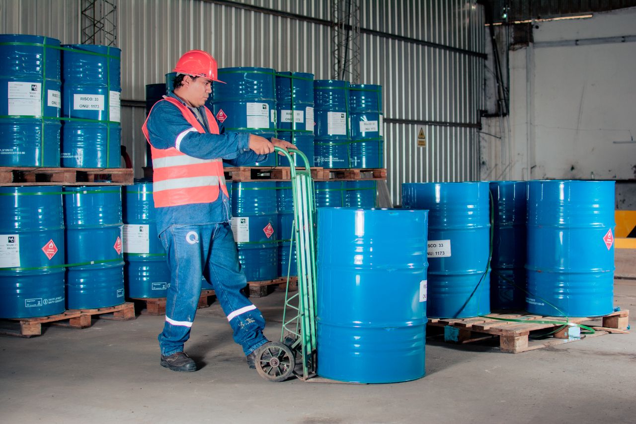 gallery-3 Industrial worker with a hand truck moving blue barrels in a warehouse setting.