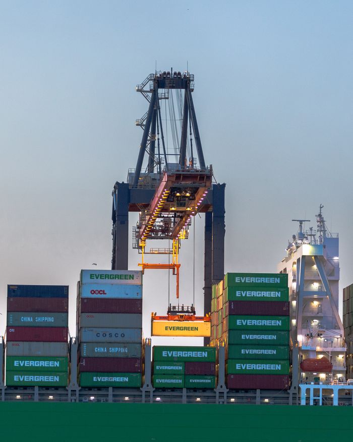 our-services-1 A busy container crane in Rotterdam port handling international cargo operations at dusk.
