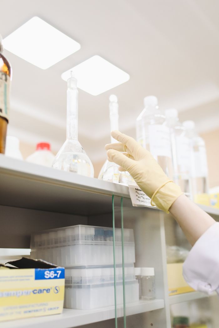 about-02 Scientist's gloved hand reaching for a beaker in a laboratory setting, showcasing research precision.