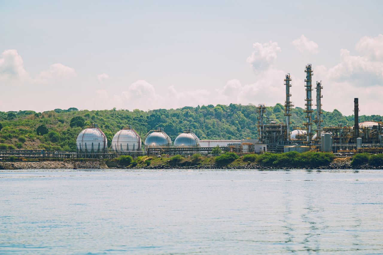 gallery-6 A scenic view of a coastal industrial gas storage facility with spherical tanks and tall chimneys.